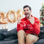 Excited winner sitting on sofa with balloons and christmas tree behind