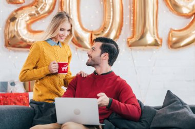 Yeni yıl için 2019 altın balonlu evde kanepede oturmuş kahve ile kadın ise dizüstü kullanan adam