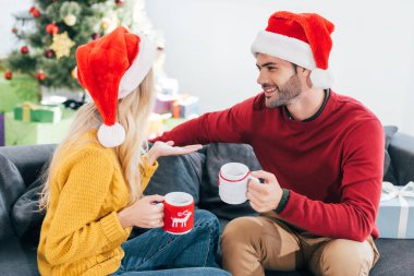 İki bardak kahve tutarak ve birbirine bakarak Noel arifesinde Noel Baba şapkaları içinde