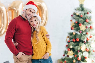 evde sarılma ile Noel ağacı Noel Baba şapkaları mutlu genç çift