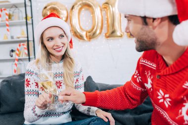 İki şampanya bardağı ile toasting ve yeni yıl evde kutlama Noel Baba şapkaları içinde gülümseyen