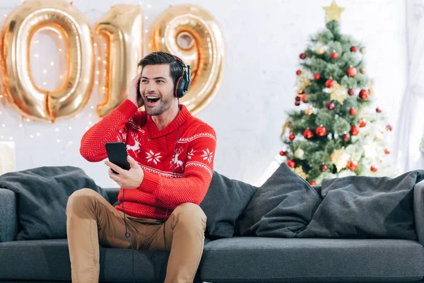 excited man listening music with headphones and smartphone on christmas eve