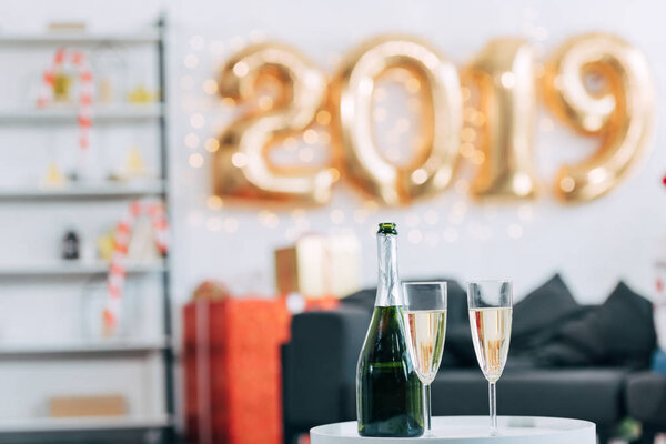 бутылка шампанского и бокалы с шариками 2019 года на заднем плане
