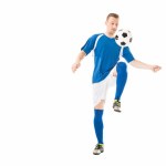 Атлетичный молодой спортсмен в футбольной форме тренируется с мячом, изолированным по белому Атлетичный молодой спортсмен в футбольной форме тренируется с мячом, изолированным по белому