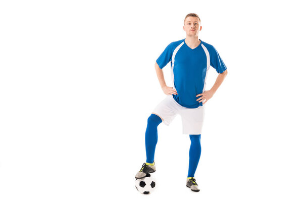 confident young soccer player standing with hands on hips and looking at camera isolated on white