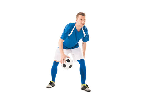 full length view of smiling young sportsman playing with soccer ball isolated on white