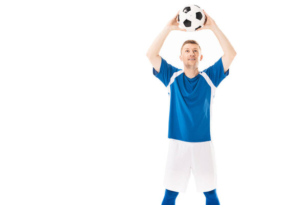 smiling young soccer player holding ball above head and looking up isolated on white