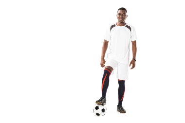 futbol topuyla duran ve üzerinde beyaz izole kamera gülümseyen yakışıklı genç Afro-Amerikan sporcu