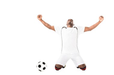 triumphing young african american soccer player kneeling near ball isolated on white  clipart