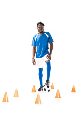 marker koni arasında futbol topu ile ayakta ve üzerinde beyaz izole kamera gülümseyen genç Afro-Amerikan sporcu