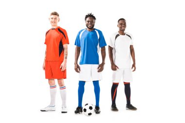 birlikte duran ve üzerinde beyaz izole kamera gülümseyen mutlu genç atletik çok ırklı futbol oyuncuları