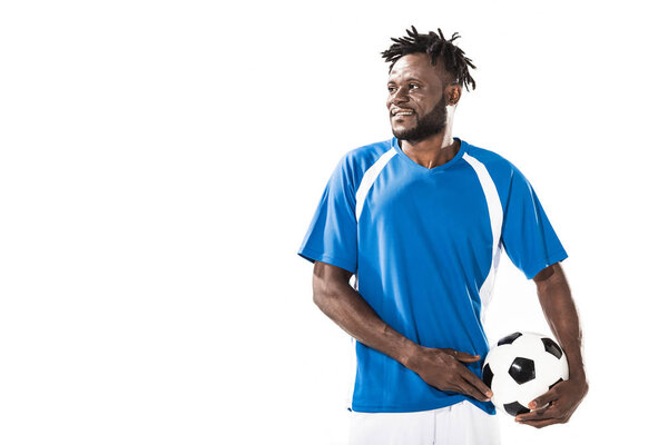 handsome smiling african american soccer player holding ball and looking away isolated on white