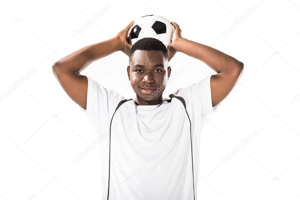young african american soccer player holding ball above head and smiling at camera isolated on white 