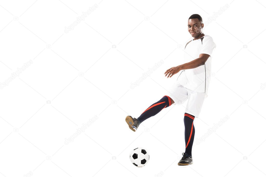 young african american soccer player kicking ball and smiling at camera isolated on white