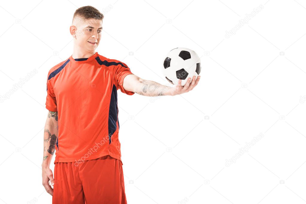 smiling young soccer player looking at ball on hand isolated on white