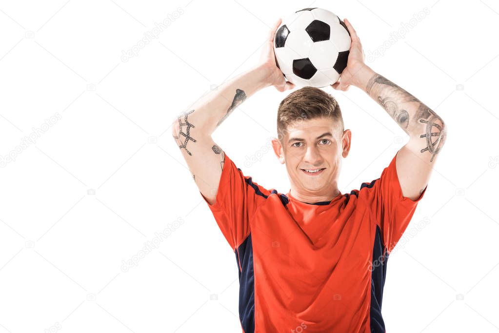 handsome young sportsman holding soccer ball above head and smiling at camera isolated on white