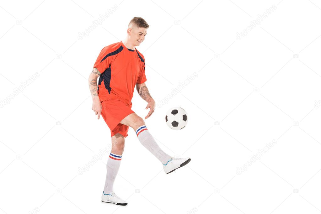 full length view of smiling young sportsman kicking soccer ball isolated on white 