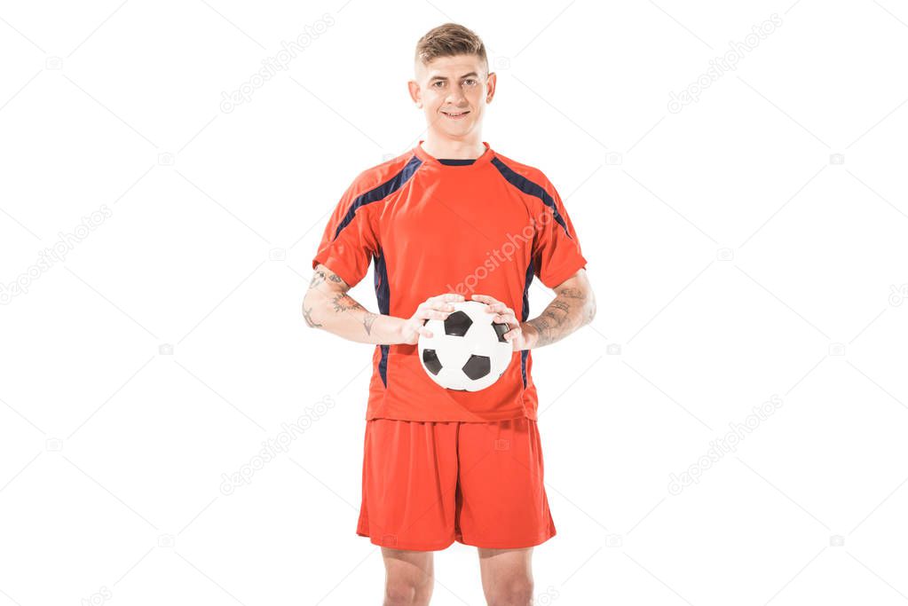 handsome young soccer player holding ball and smiling at camera isolated on white