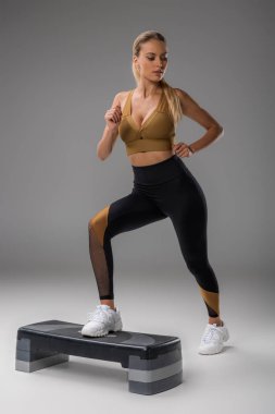 sportive young woman exercising on step board on grey