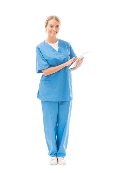 smiling young nurse working with digital tablet and looking at camera isolated on white