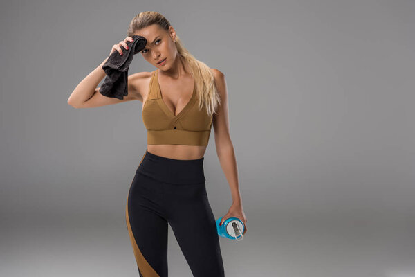 атлетичная молодая женщина вытирает пот о лоб полотенцем на сером
