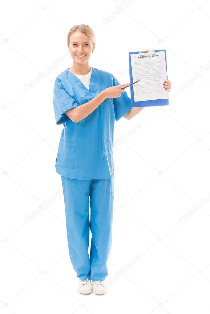 smiling young nurse pointing at clipboard with insurance form isolated on white