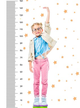 happy kid in eyeglasses standing on pile of books to be higher isolated on white with stars and growth measures clipart