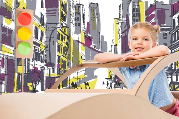 adorable child playing with cardboard car and traffic lights on street in drawn city