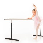 Little ballerina in tutu stretching leg at ballet barre stand isolated on white background