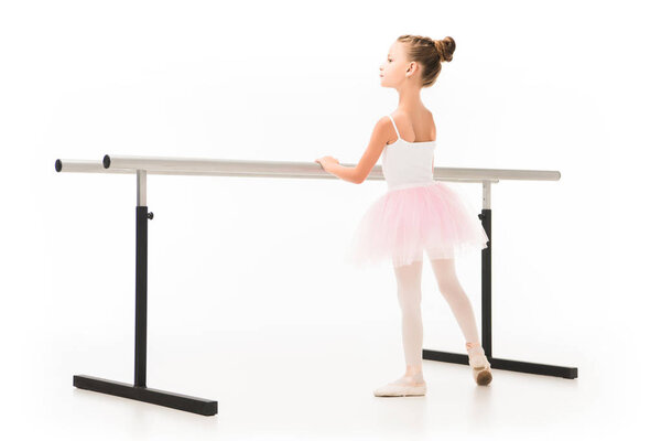 rear view of beautiful little ballerina in tutu exercising at ballet barre stand isolated on white background 