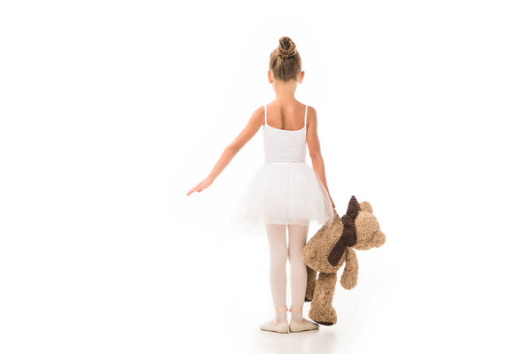 rear view of little ballerina in tutu practicing with teddy bear isolated on white background 