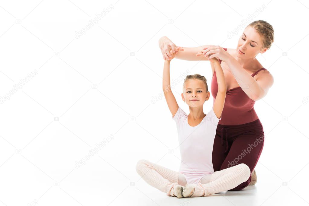 serious female trainer helping little kid exercising isolated on white background 