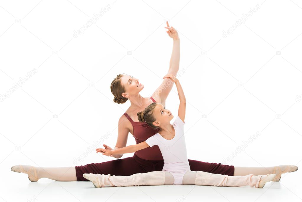 smiling female teacher showing exercise to little ballerina sitting on twine isolated on white background 