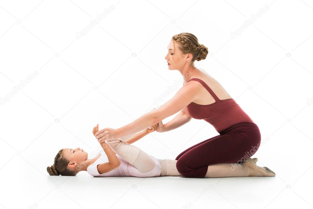 confident female trainer helping little ballerina stretching isolated on white background 