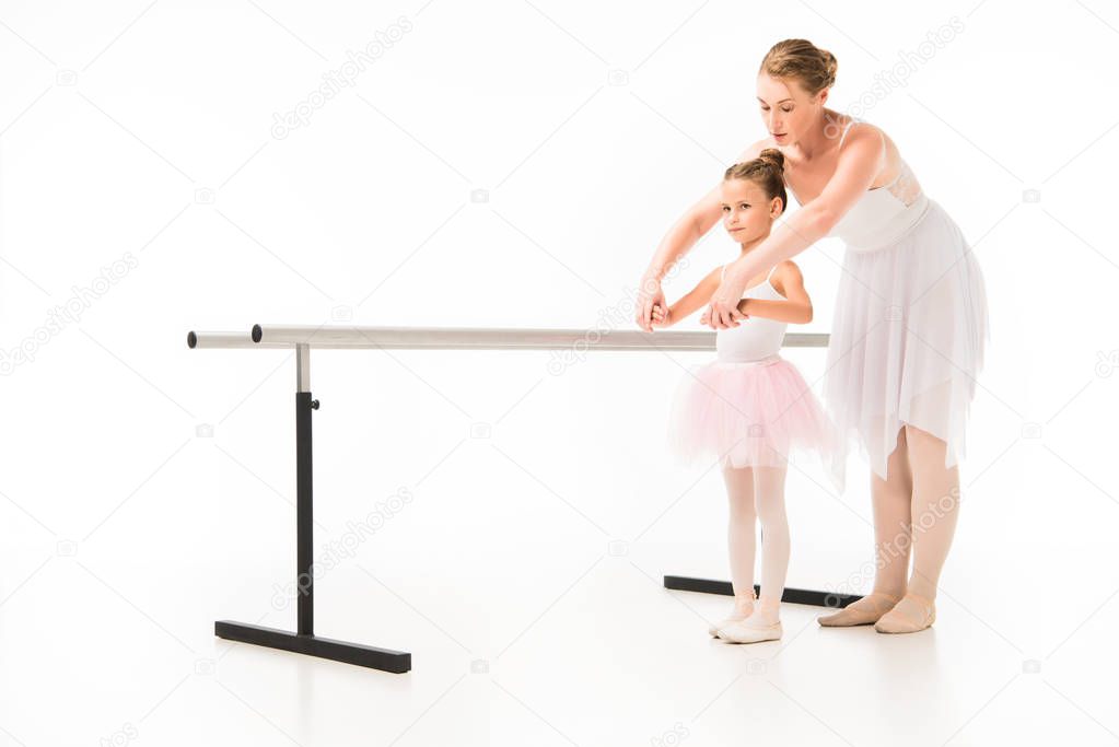 female teacher in tutu helping little ballerina practicing at ballet barre stand isolated on white background 