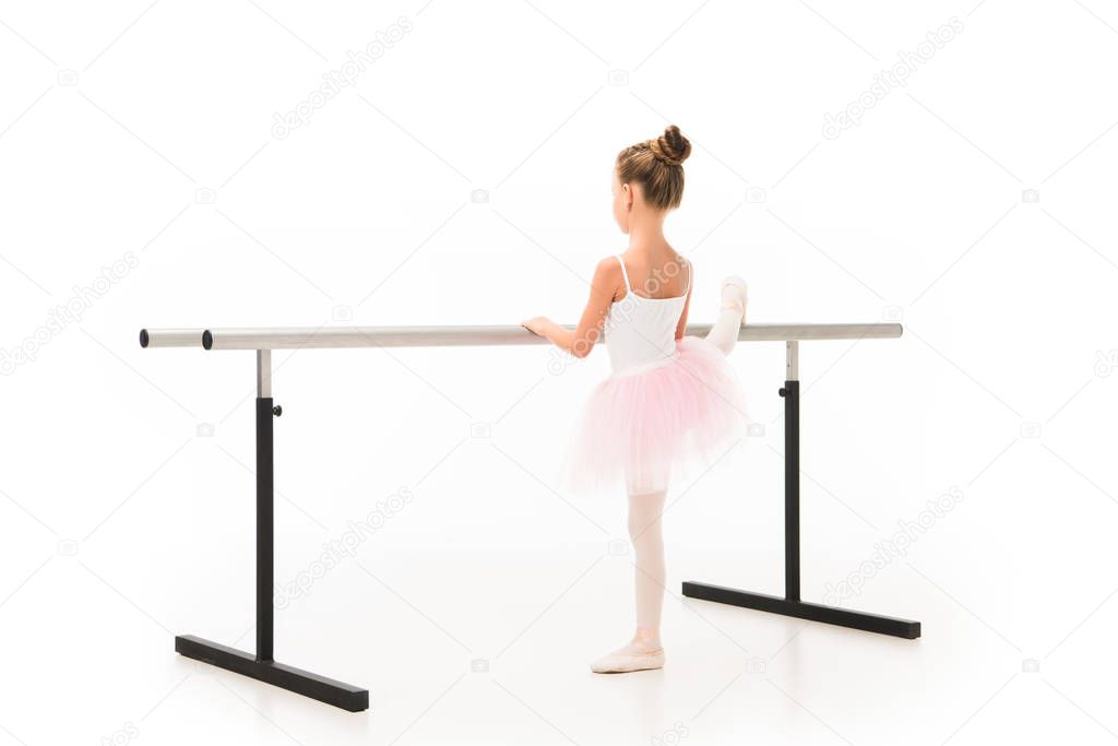 rear view of little ballerina in tutu and pointe shoes exercising at ballet barre stand isolated on white background 
