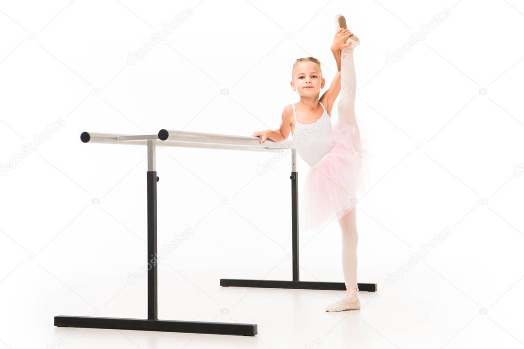 beautiful little ballerina in tutu and pointe shoes stretching at ballet barre stand isolated on white background 