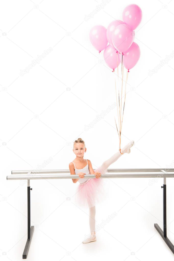adorable little ballerina in tutu practicing with pink balloons wrapped over her at ballet barre stand isolated on white background 