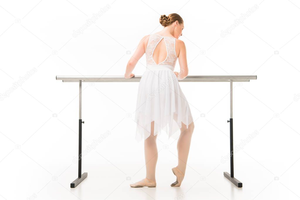 rear view of adult ballerina in tutu exercising at ballet barre stand isolated on white background 