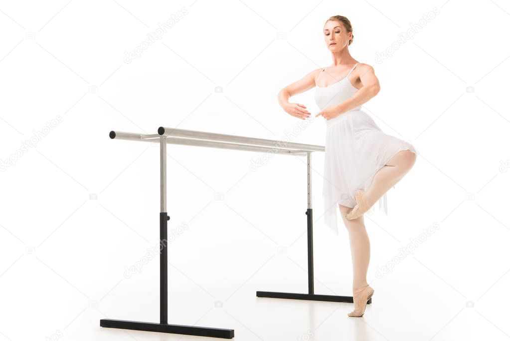 focused ballerina in tutu and pointe shoes practicing at ballet barre stand isolated on white background 