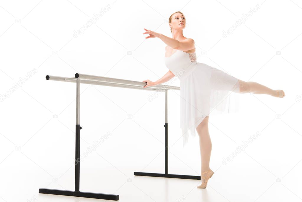 beautiful ballerina in tutu and pointe shoes exercising at ballet barre stand isolated on white background 