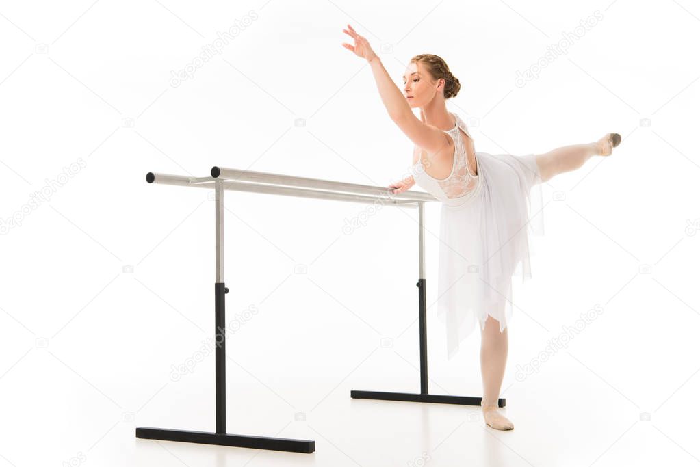 adult ballerina in tutu and pointe shoes exercising at ballet barre stand isolated on white background 