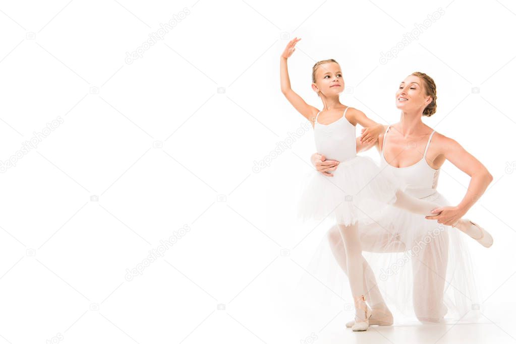 smiling adult female coach helping little ballerina exercising isolated on white background 