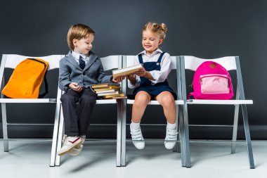 kitap tutan ve sırt çantaları ile sandalyelere oturan sevimli sınıf