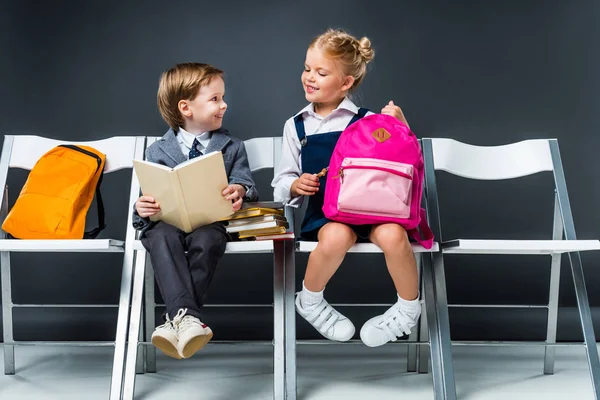 Glimlachend Klasgenoten Zitten Stoelen Met Boeken Rugzakken Terwijl Schooljongen Leesboek — Stockfoto