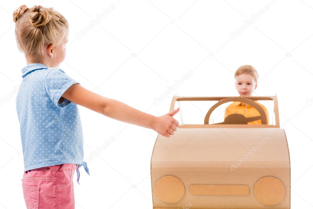 adorable kid hitchhiking while boy driving cardboard car, isolated on white