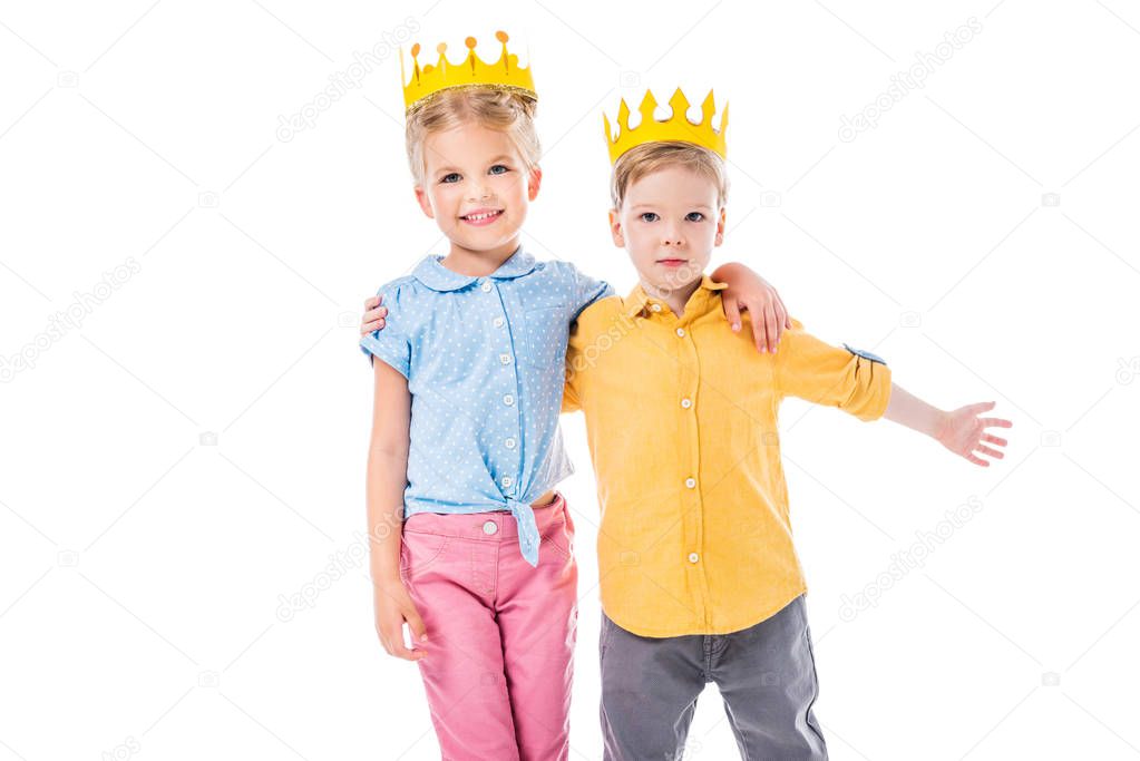 adorable kids in yellow paper crowns hugging and looking at camera, isolated on white