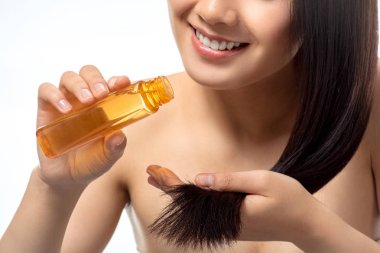 cropped shot of smiling woman pouring oil on split ends isolated on white clipart