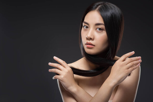 portrait of young asian woman with beautiful and healthy dark hair looking at camera isolated on black