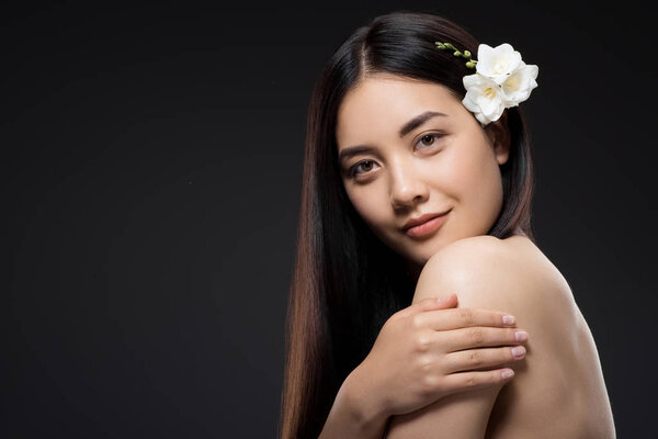 portrait of beautiful young asian woman with white flowers in hair looking at camera isolated on black